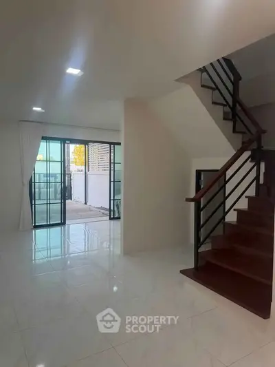 Spacious modern living room with staircase and large windows leading to balcony.