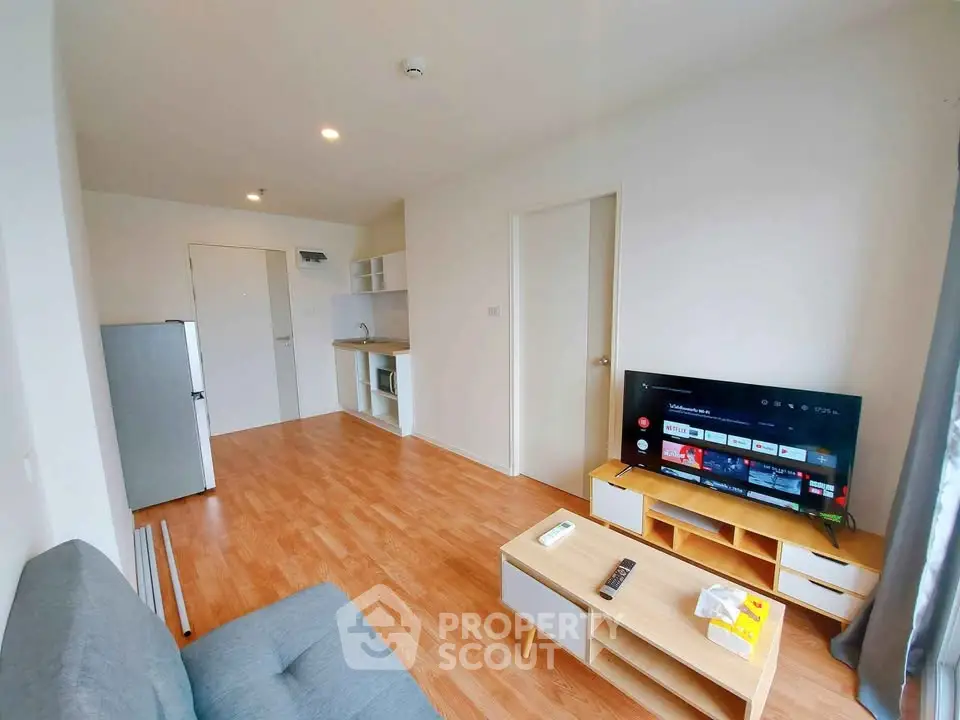 Modern living room with wooden flooring, cozy sofa, and entertainment setup in a bright apartment.