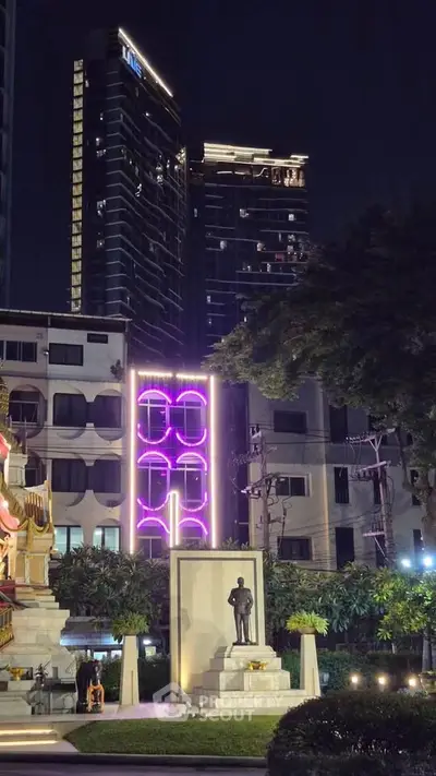 Stunning night view of modern high-rise buildings with vibrant neon lights and a statue in the foreground.
