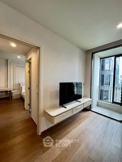 Modern apartment interior with TV and balcony view, featuring sleek wooden flooring and bright natural light.
