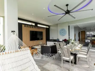 Luxurious open-plan living room with modern decor and dining area, featuring a large ceiling fan and hammock.