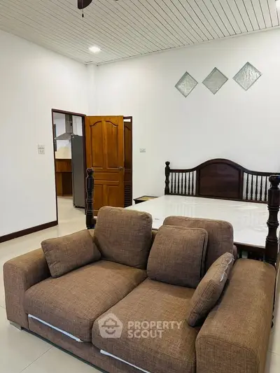 Spacious living area with cozy brown sofa and elegant wooden bed, perfect for modern living.