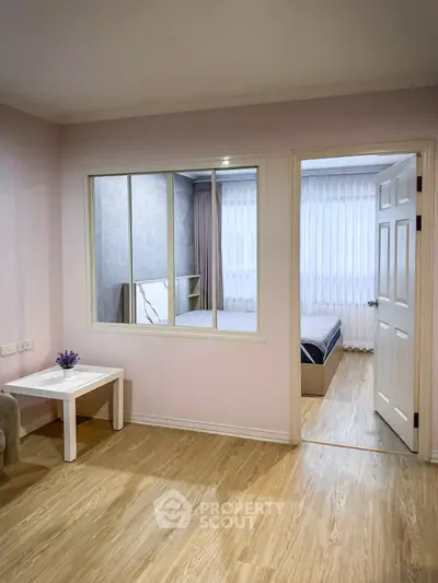 Charming interior with a cozy bedroom view through a window, featuring elegant wood flooring and soft pastel walls.