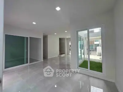 Spacious modern living room with large windows and sleek tile flooring, offering abundant natural light.