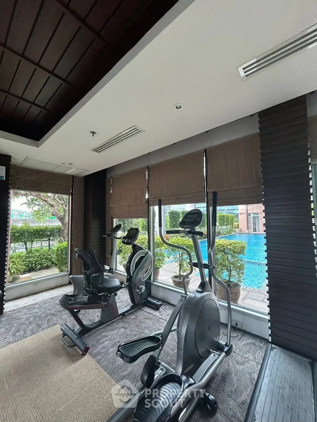 Modern gym with exercise equipment and pool view in luxury real estate property.