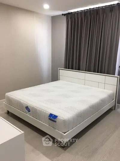 Spacious and modern bedroom with a large comfortable bed, elegant dark curtains, and soft ambient lighting, perfect for relaxation and restful sleep.