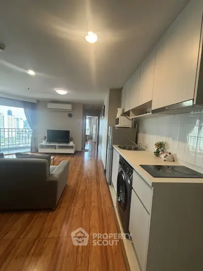 Modern open-layout living room and kitchen with city view, featuring sleek appliances and wooden flooring.