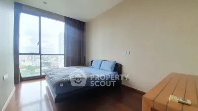 Spacious bedroom with large window offering stunning city views, featuring a cozy bed and elegant wooden flooring.