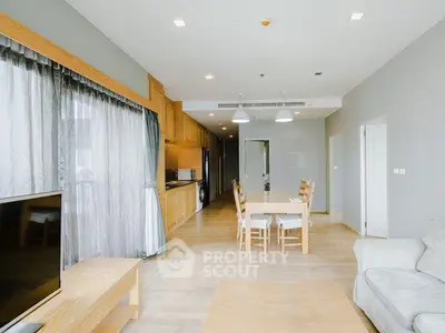 Spacious modern living room with open kitchen and dining area, featuring elegant wooden furniture and natural light.