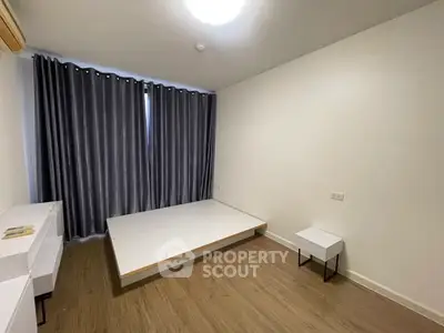 Minimalist bedroom with platform bed and modern furniture, featuring sleek wooden flooring and dark curtains.