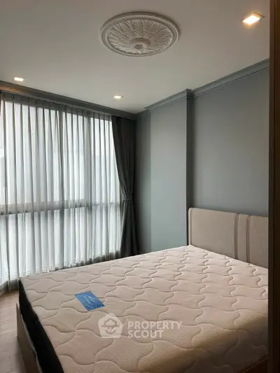 Modern bedroom with elegant ceiling design and large windows for natural light.