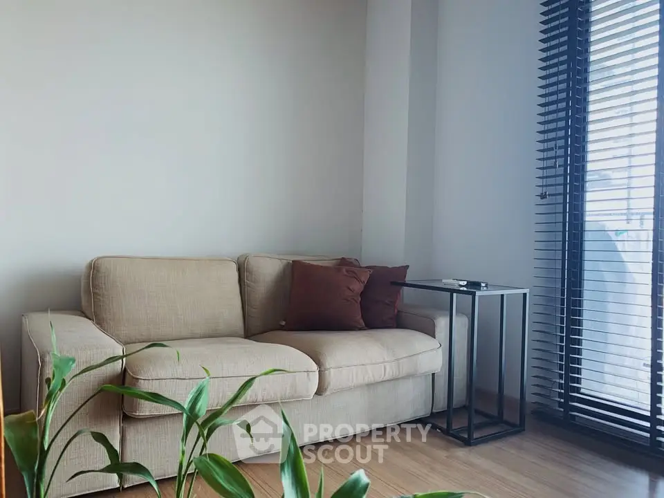 Cozy living room with beige sofa, modern blinds, and indoor plant for a serene ambiance.