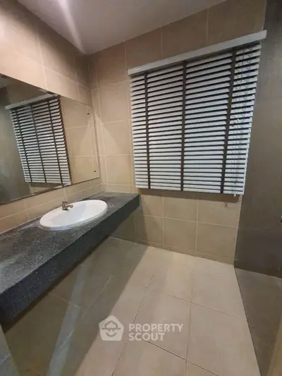 Modern bathroom with sleek sink and large mirror, featuring stylish blinds and neutral tiles.