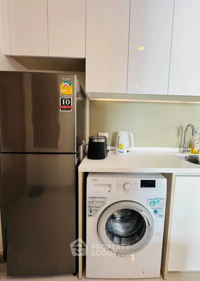 Modern kitchen with stainless steel fridge and washing machine in sleek cabinetry.