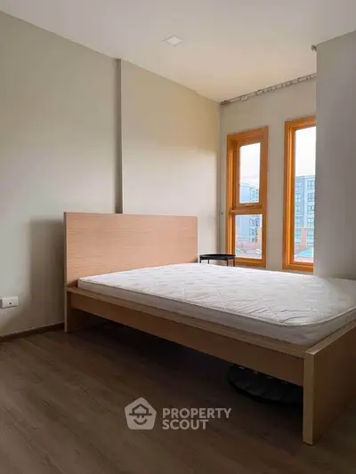 Modern bedroom with large windows and wooden flooring, offering natural light and a cozy atmosphere.