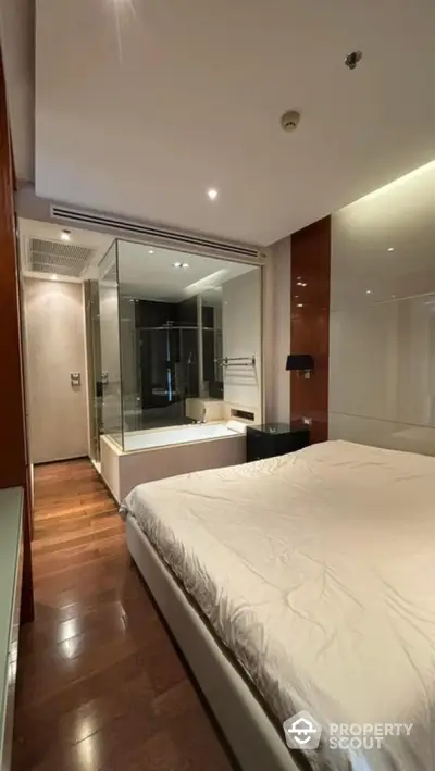 Modern bedroom with glass-enclosed bathtub and wooden flooring