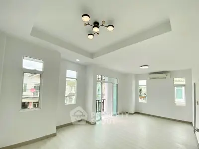 Spacious modern living room with large windows and balcony access, featuring stylish ceiling lights and air conditioning.