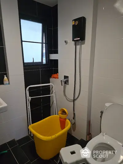 Modern bathroom with black and white tiles, featuring a shower and yellow bucket.