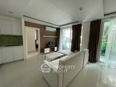 Spacious modern living room with white sofa, TV, and large windows overlooking greenery.