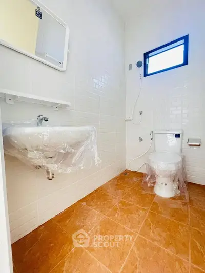 Modern bathroom with white tiles and orange floor, featuring a sink and toilet wrapped in protective plastic.