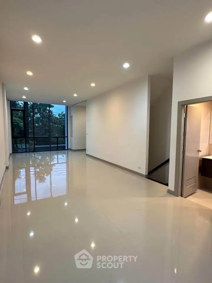 Spacious modern living room with large windows and glossy tiled floors.