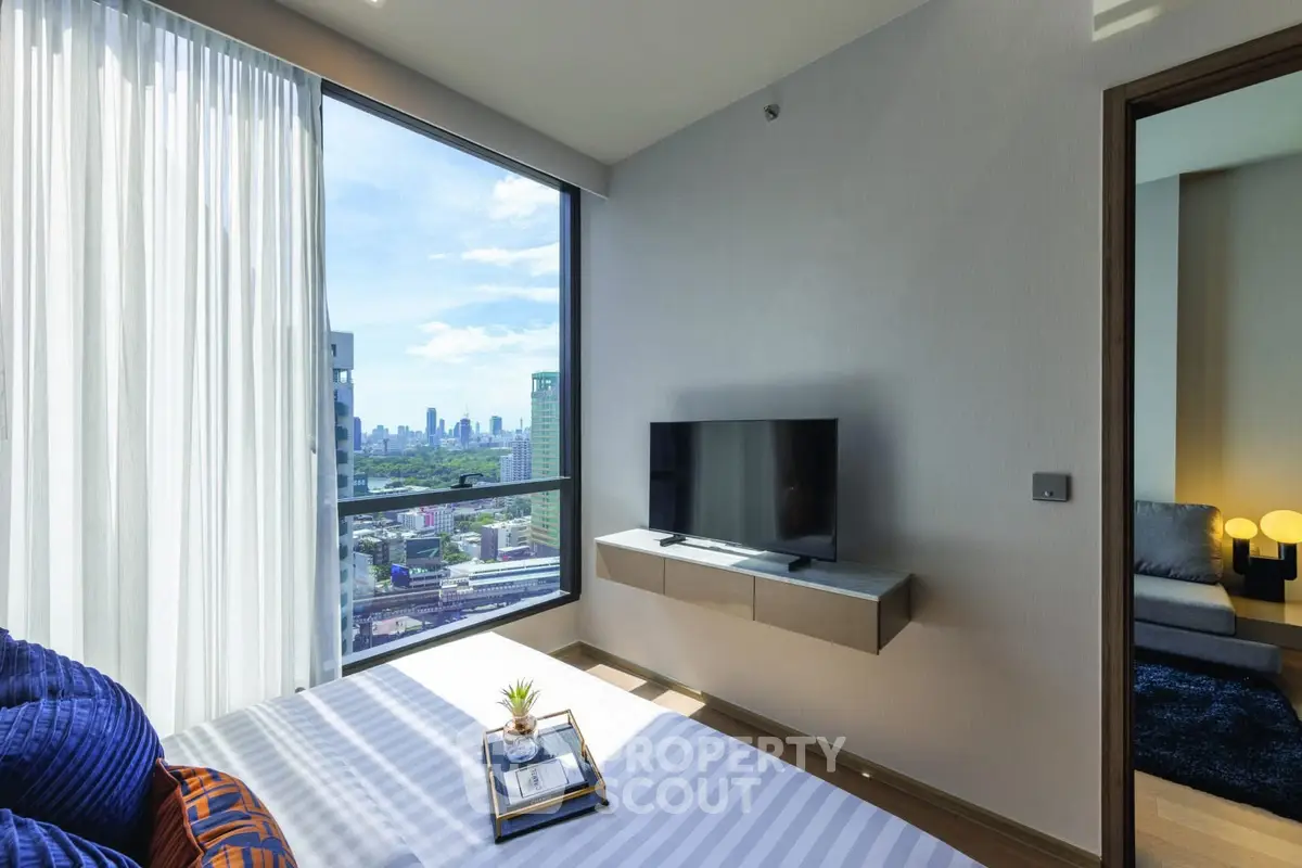 Modern bedroom with city view, featuring a sleek TV setup and stylish decor.