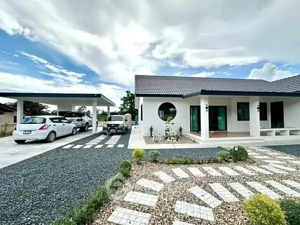Modern single-story house with spacious driveway and landscaped garden under a bright sky.