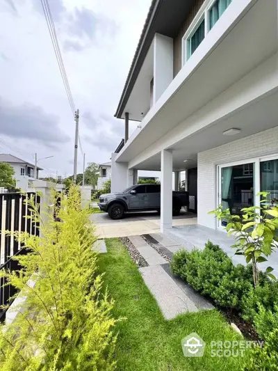 Modern two-story house with sleek design and spacious driveway, surrounded by lush greenery and a well-maintained garden.