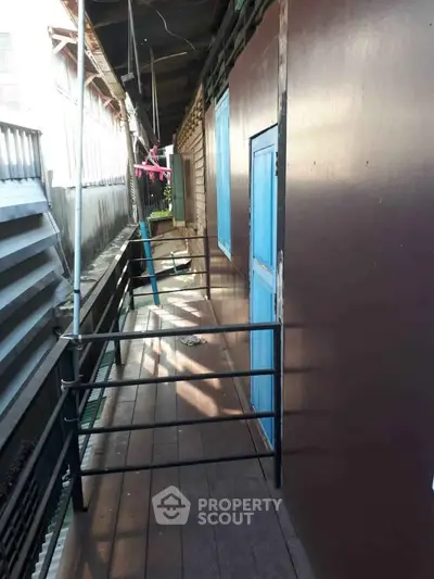 Narrow balcony with metal railing and blue doors in a residential setting.
