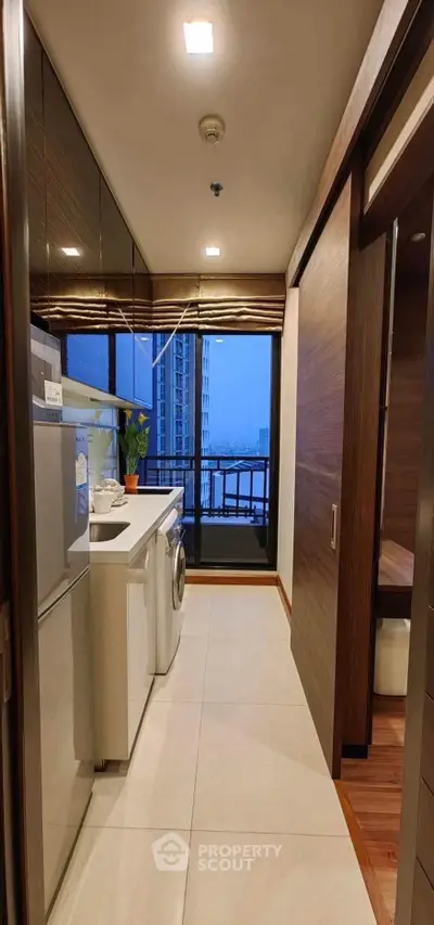 Modern kitchen with washing machine and balcony view in high-rise apartment.