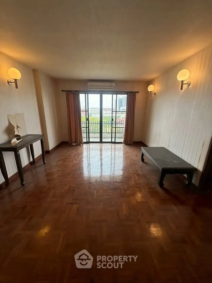 Spacious living room with parquet flooring and large windows opening to a balcony.