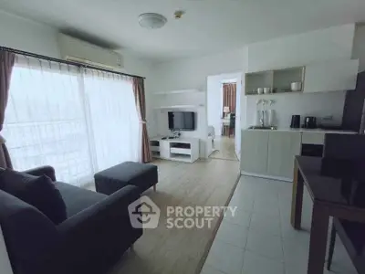 Modern living room with open kitchen and natural light, featuring stylish furniture and appliances.