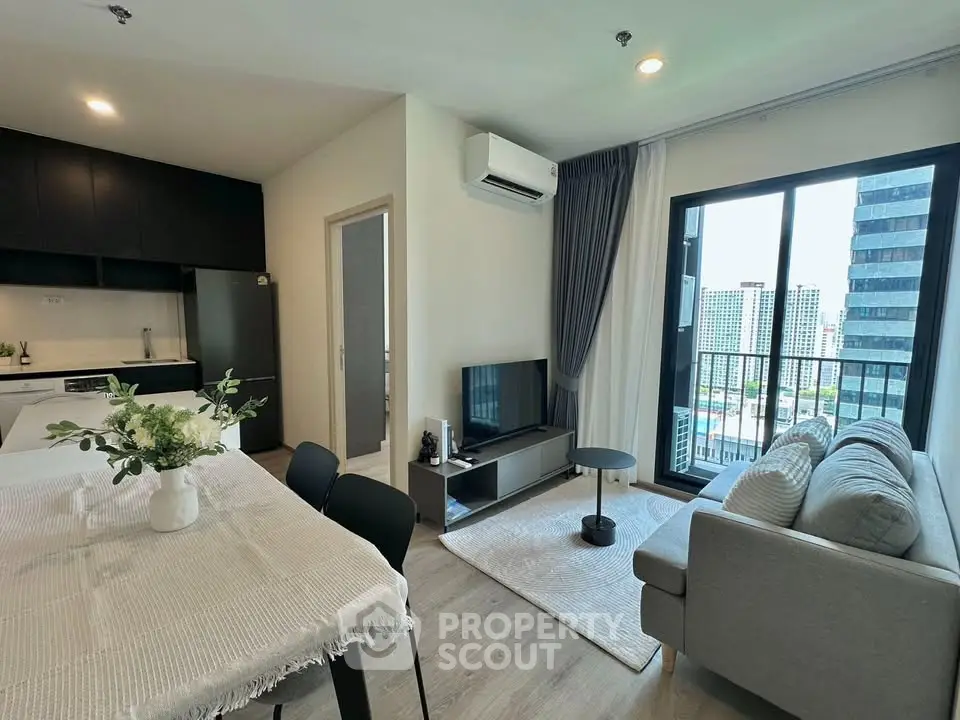 Modern living room with city view, stylish furniture, and open kitchen layout in a high-rise apartment.
