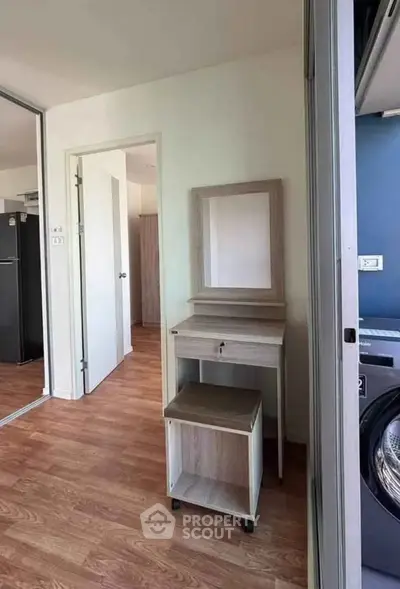 Modern apartment interior with wooden flooring and compact furniture, featuring a washing machine and refrigerator.