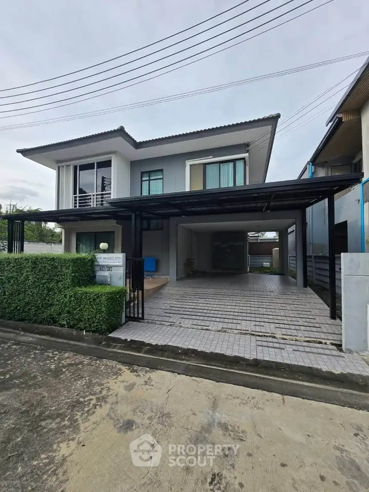 Modern two-story house with carport and lush greenery in a serene neighborhood.