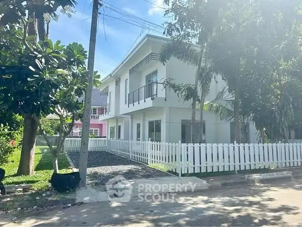 Charming two-story white house with picket fence and lush greenery