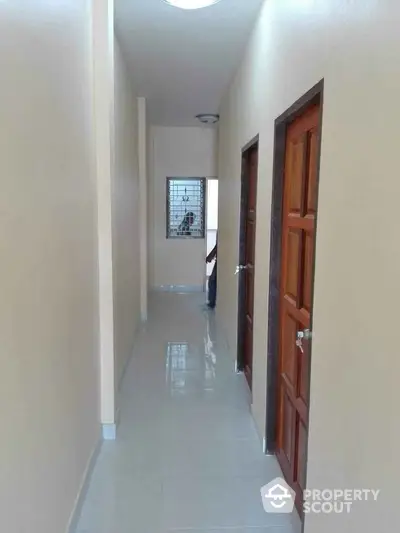 Bright hallway with polished tile flooring and wooden doors, leading to a window with a view of the outdoors.