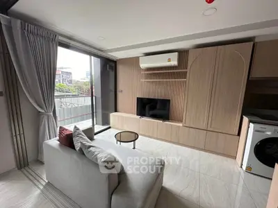 Modern living room with sleek design, featuring a cozy sofa, TV, and washing machine, opening to a balcony view.