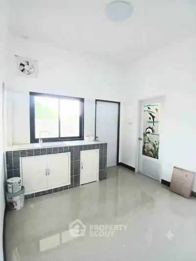Spacious kitchen with modern design and ample natural light, featuring sleek countertops and a large window.