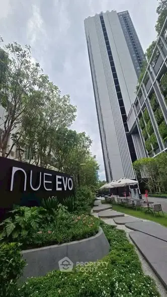 Modern high-rise building with lush garden pathway and outdoor seating area.