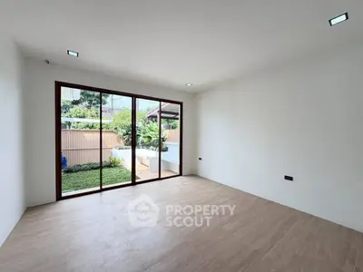 Spacious empty room with large sliding glass doors opening to a lush garden, perfect for customization.