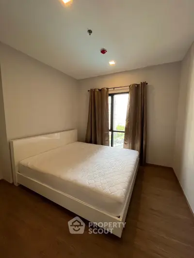 Spacious bedroom with large window and elegant curtains in modern apartment.