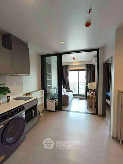 Modern apartment with open kitchen and cozy living area, featuring a washing machine and large windows.
