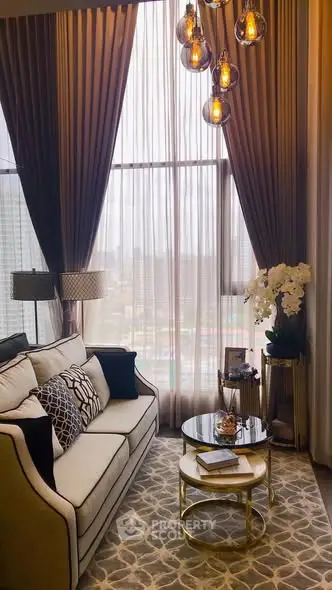 Luxurious living room with high ceilings, elegant chandelier, and floor-to-ceiling windows offering city views.