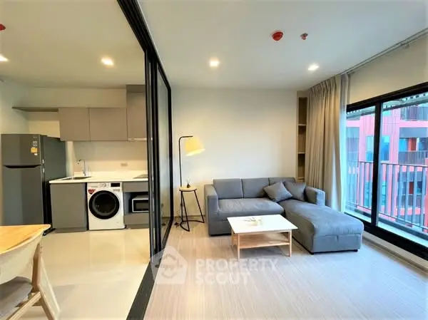 Modern open-plan living room with kitchen, featuring cozy sofa and natural light.