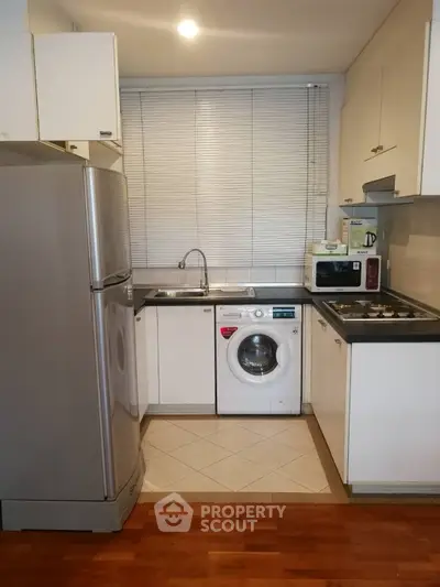 Modern kitchen with appliances including fridge, washing machine, and microwave in compact layout.