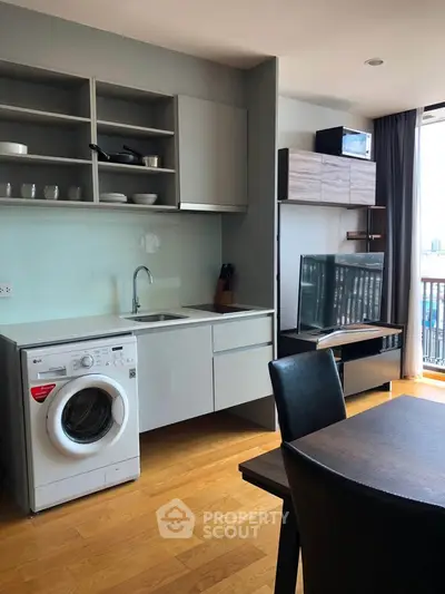 Modern apartment kitchen with washing machine and open shelving, featuring a sleek TV setup and dining area.