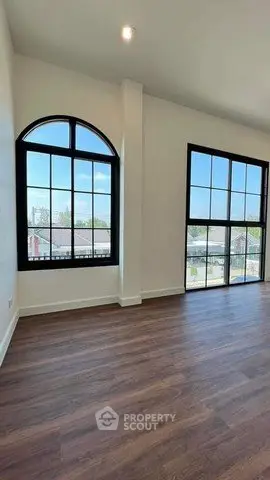 Spacious living room with large arched windows and wooden flooring, offering ample natural light.