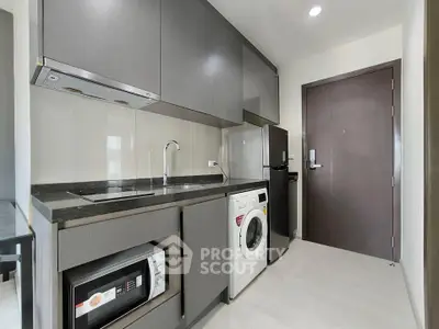 Modern kitchen with sleek cabinets, washing machine, and microwave in compact layout.