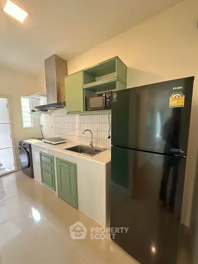 Modern kitchen with green cabinets, sleek black fridge, and built-in microwave in a stylish apartment.